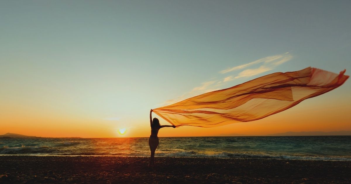 silhouette of woman holding a large fabric blowing in wind