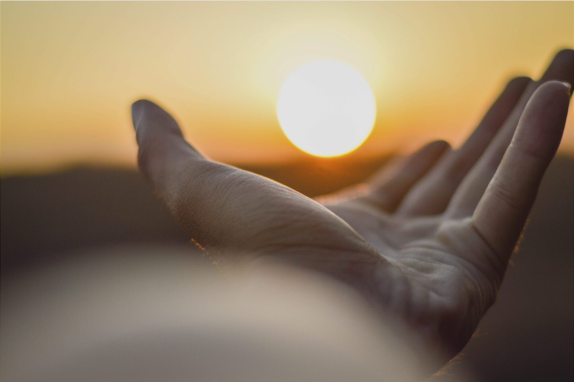 Image of person's hand seeming holding setting sun as it lowers to horizonsetting sun