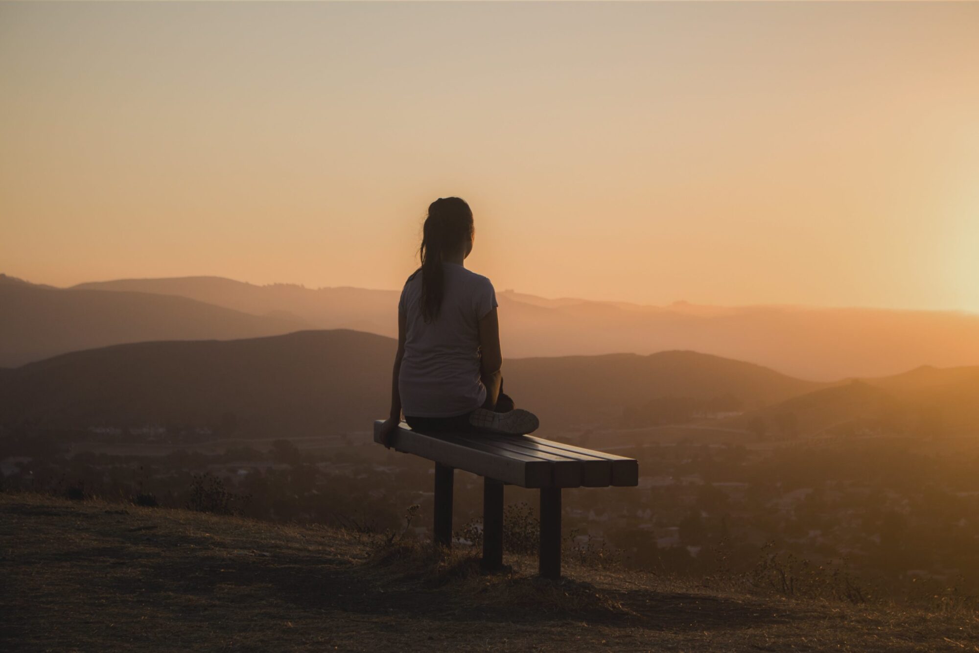 Silhouette of woman on a bench on a hill at sunset