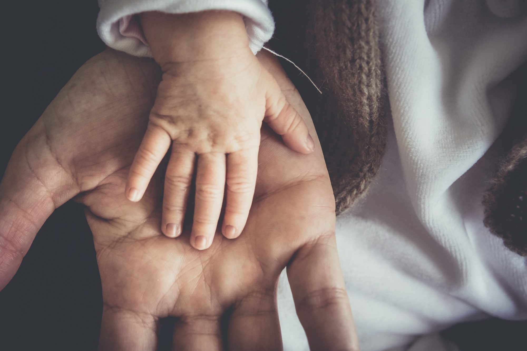 Heartfelt image of baby's hand on top of an adult male's hand